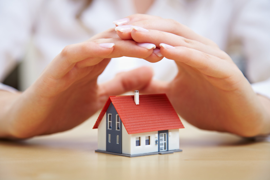 woman's hand protecting a miniature house in the table